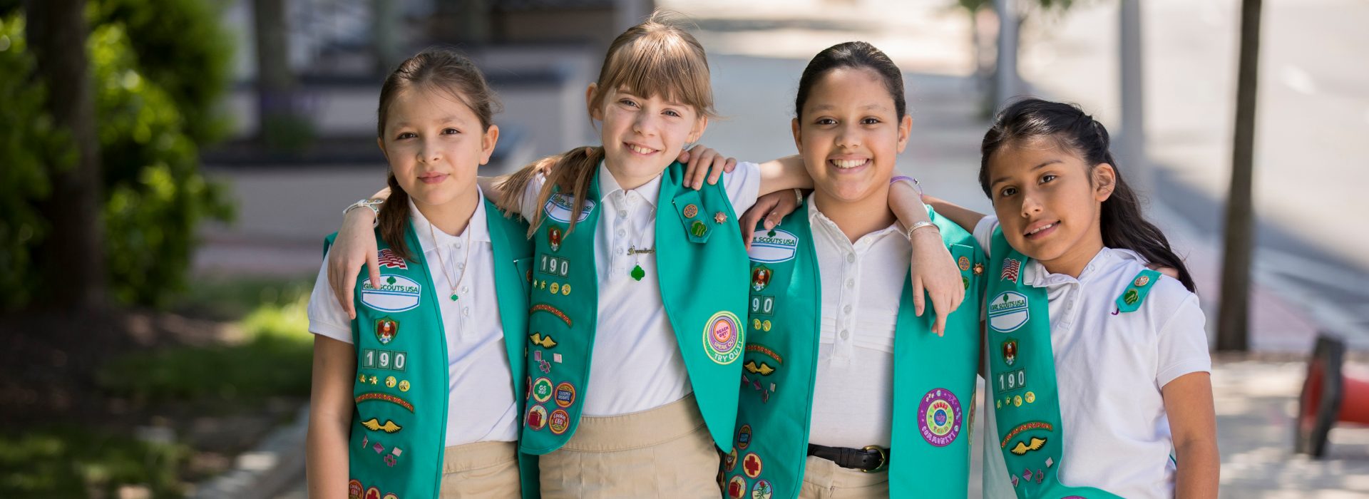  two girl scout juniors outside wearing junior vest uniform smiling and hugging 